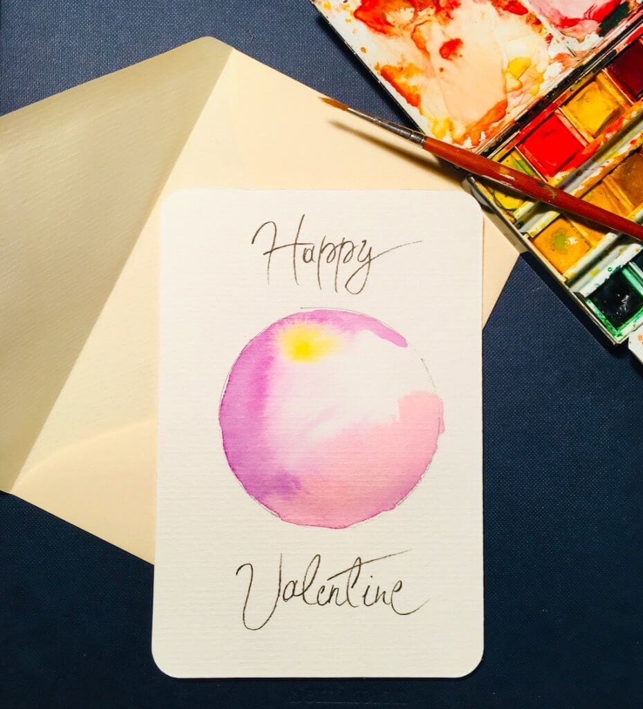 Man sieht die fertige Valentins-Karte, gemalt von der Künstlerin Dodo Kresse. Es ist eine rosa-gelbe Scheibe aus Aquarellfarbe und trägt den Titel Happy Valentine. 