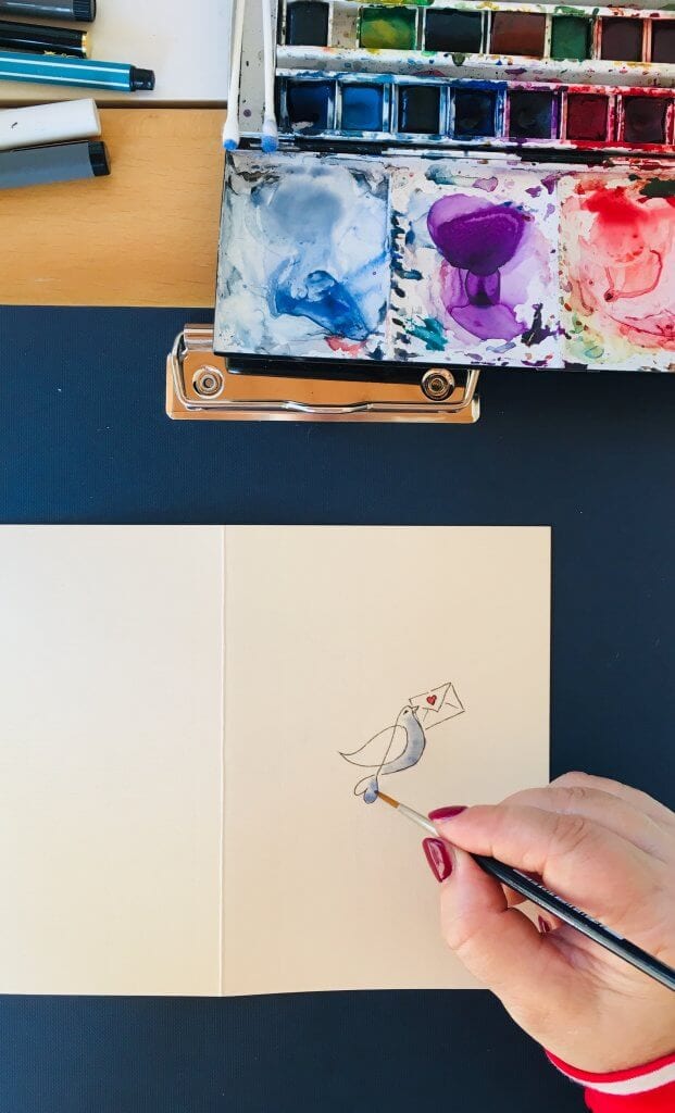 Man sieht das Einfärben der Taube auf der Valentinskarte mit Aquarellfarben, hier ein dunkles Blau. 